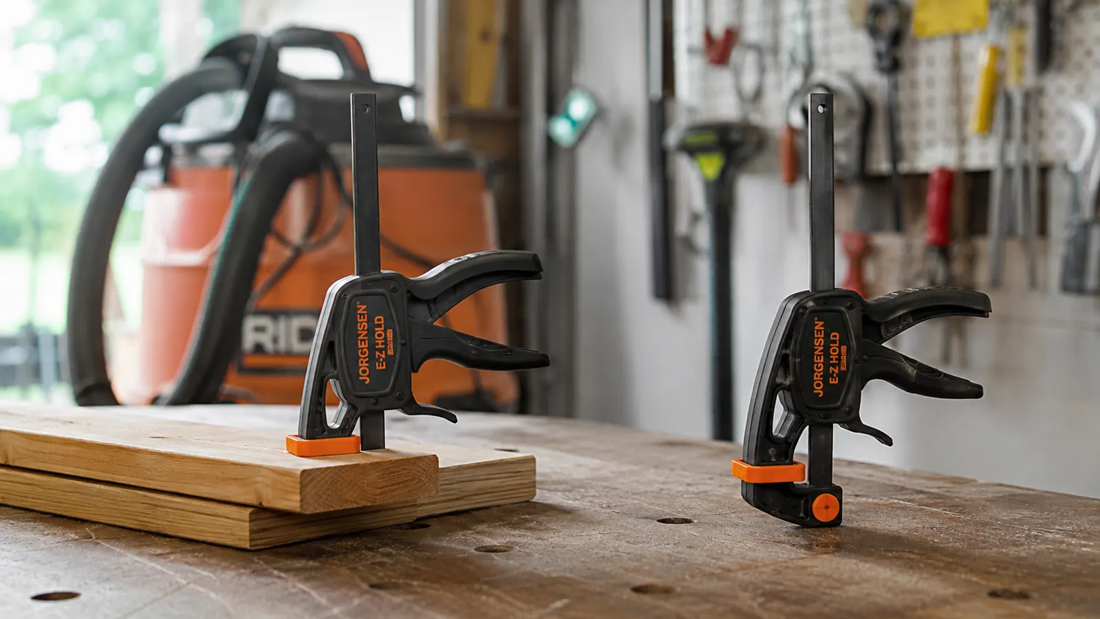 A small clamp holding two pieces of wood together on a workbench, with a second clamp standing nearby